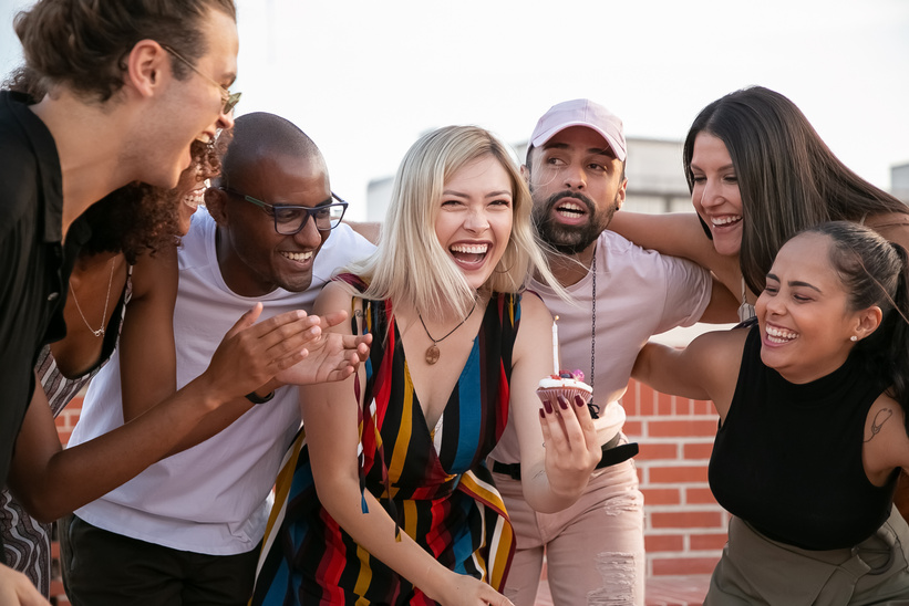 Excited young diverse friends celebrating birthday of cheerful woman on terrace